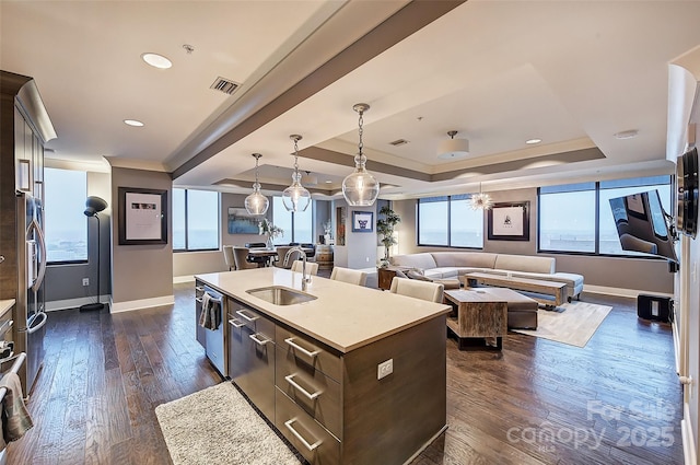 kitchen featuring sink, decorative light fixtures, a raised ceiling, an island with sink, and dark brown cabinets