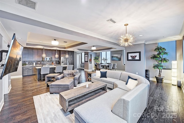 living area with dark wood finished floors, a raised ceiling, visible vents, and an inviting chandelier