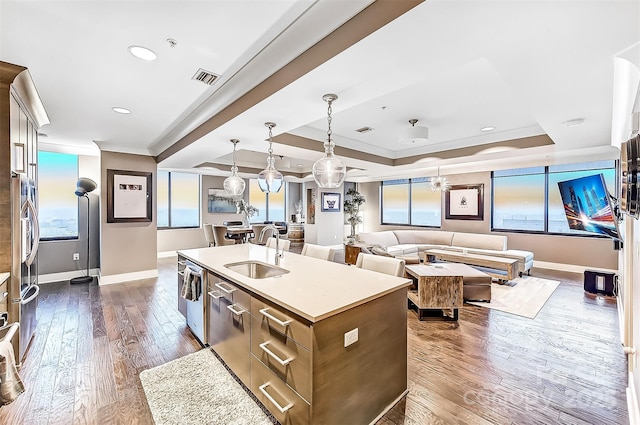 kitchen with a raised ceiling, an island with sink, open floor plan, light countertops, and a sink