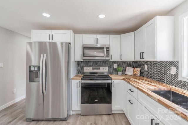 kitchen with butcher block countertops, white cabinets, and appliances with stainless steel finishes