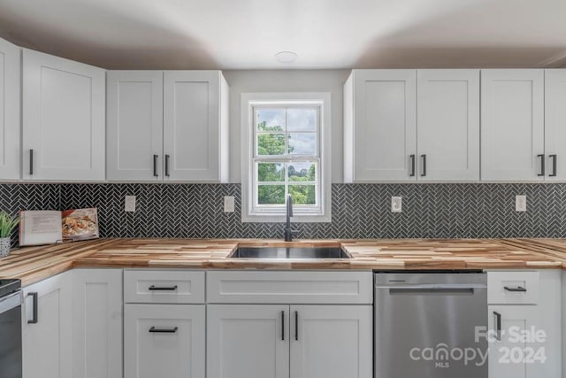 kitchen with butcher block countertops, sink, stainless steel dishwasher, and white cabinets