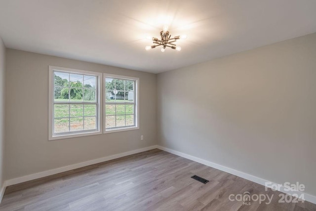 empty room featuring a notable chandelier and light wood-type flooring