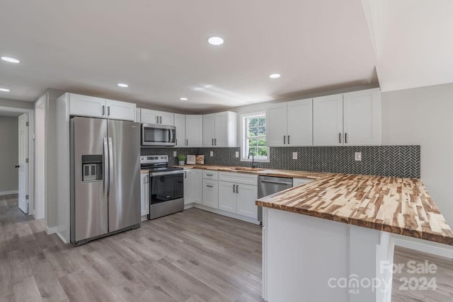 kitchen featuring butcher block countertops, sink, appliances with stainless steel finishes, white cabinets, and kitchen peninsula