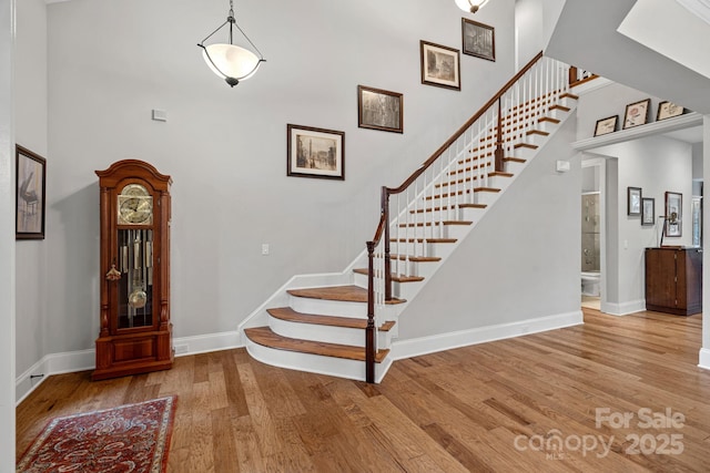 stairs with wood finished floors, a towering ceiling, and baseboards