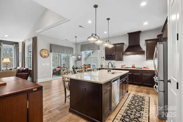 kitchen featuring a center island with sink, open floor plan, stainless steel appliances, premium range hood, and a sink