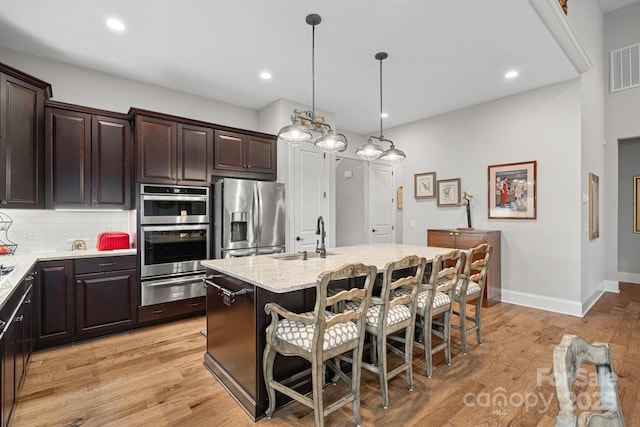 kitchen featuring a center island with sink, a warming drawer, hanging light fixtures, appliances with stainless steel finishes, and a sink