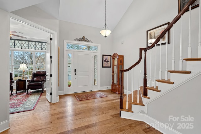 entrance foyer featuring light wood-style flooring, a ceiling fan, high vaulted ceiling, baseboards, and stairs