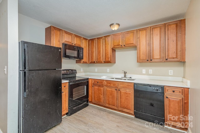 kitchen featuring brown cabinetry, light countertops, light wood-type flooring, black appliances, and a sink