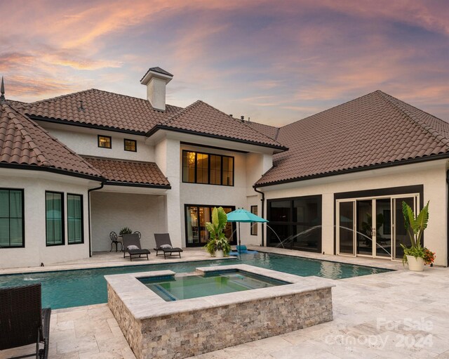 back house at dusk featuring a patio, pool water feature, and a pool with hot tub