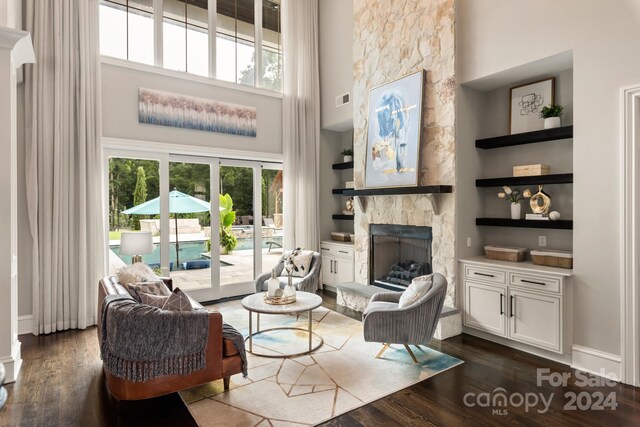 living room featuring built in features, a fireplace, a towering ceiling, and dark wood-type flooring