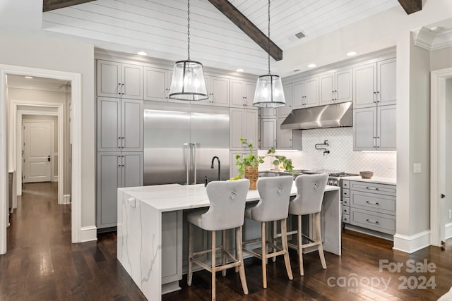 kitchen featuring beam ceiling, dark wood-type flooring, a kitchen island with sink, decorative backsplash, and built in refrigerator