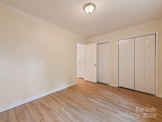 unfurnished bedroom featuring multiple closets, light wood-type flooring, and ornamental molding