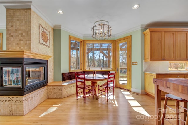 dining area featuring light wood-style floors, a chandelier, crown molding, and a multi sided fireplace