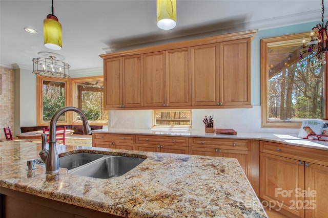 kitchen featuring brown cabinetry, ornamental molding, light stone counters, hanging light fixtures, and a sink