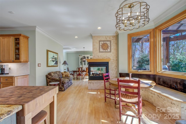 dining room featuring a chandelier, crown molding, a multi sided fireplace, and light wood-style floors