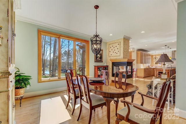 dining room featuring light wood-style flooring, recessed lighting, a multi sided fireplace, baseboards, and crown molding