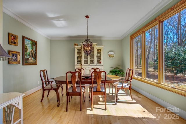 dining room with ornamental molding, light wood-type flooring, baseboards, and an inviting chandelier