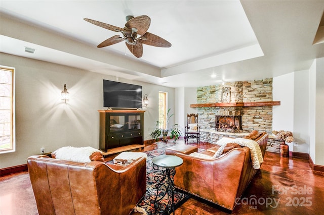 living area featuring ceiling fan, a stone fireplace, visible vents, baseboards, and a raised ceiling