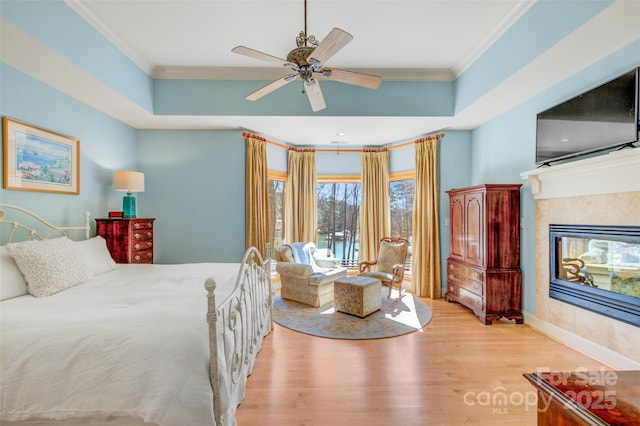 bedroom featuring wood finished floors, baseboards, a tiled fireplace, a raised ceiling, and crown molding