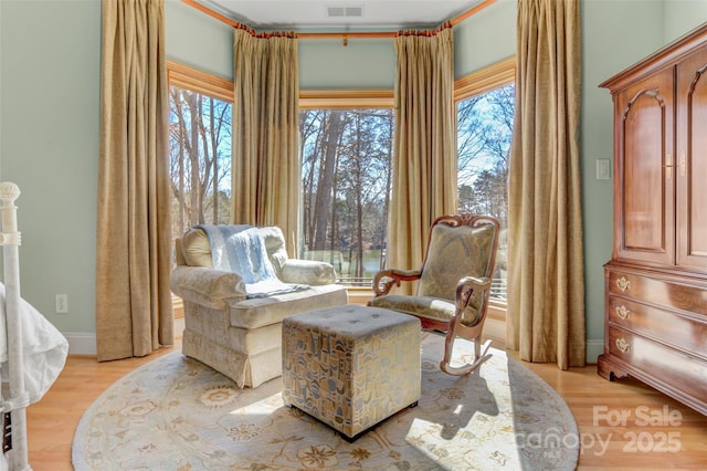 living area with light wood-style floors, a healthy amount of sunlight, visible vents, and baseboards