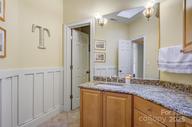 bathroom with a decorative wall, a skylight, visible vents, vanity, and wainscoting