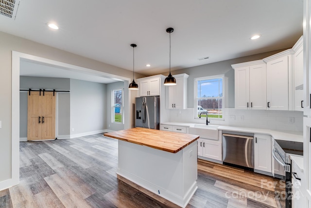 kitchen featuring white cabinetry, tasteful backsplash, a barn door, stainless steel appliances, and sink