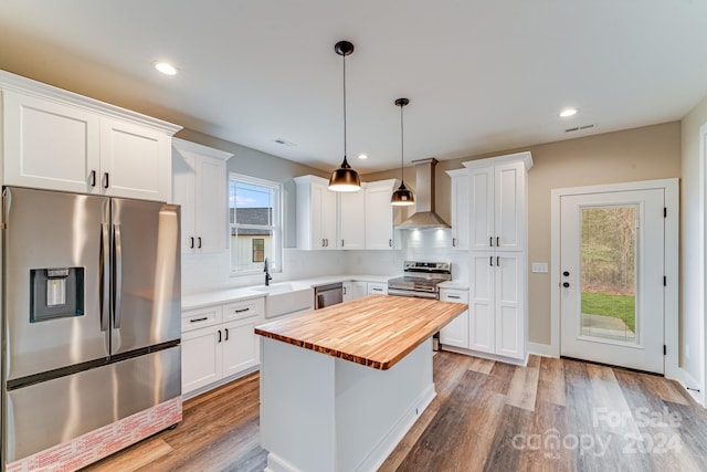 kitchen featuring appliances with stainless steel finishes, tasteful backsplash, wall chimney range hood, light wood-type flooring, and white cabinetry