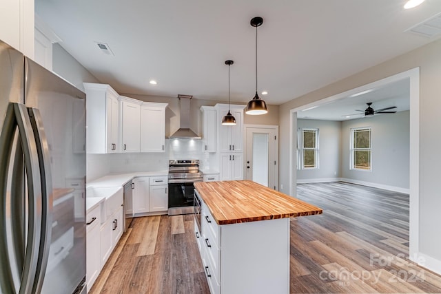 kitchen featuring tasteful backsplash, wooden counters, stainless steel appliances, wall chimney exhaust hood, and light hardwood / wood-style floors