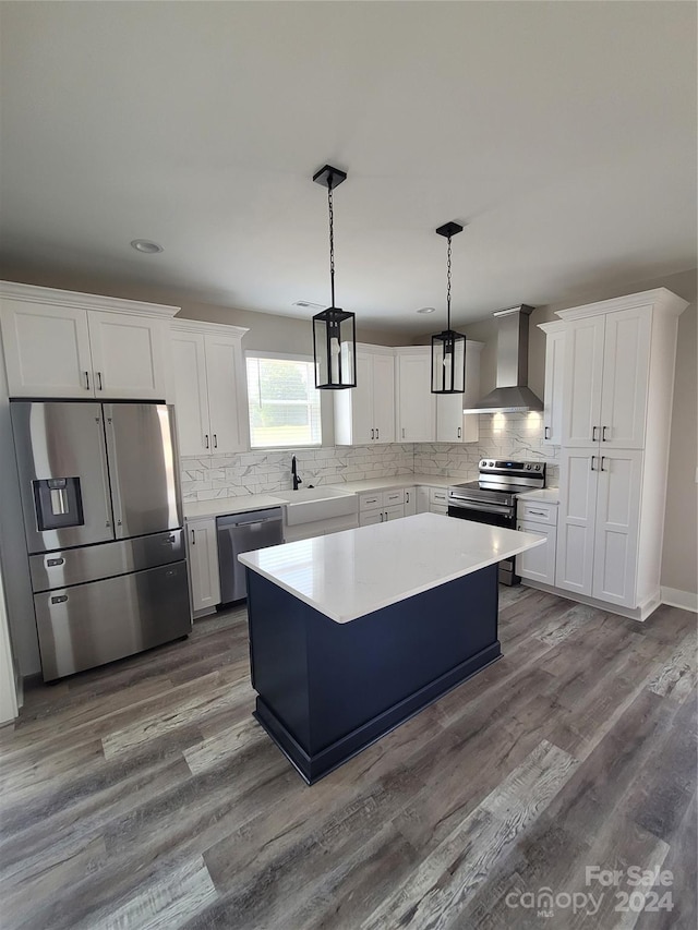 kitchen with wall chimney range hood, a kitchen island, pendant lighting, appliances with stainless steel finishes, and hardwood / wood-style flooring