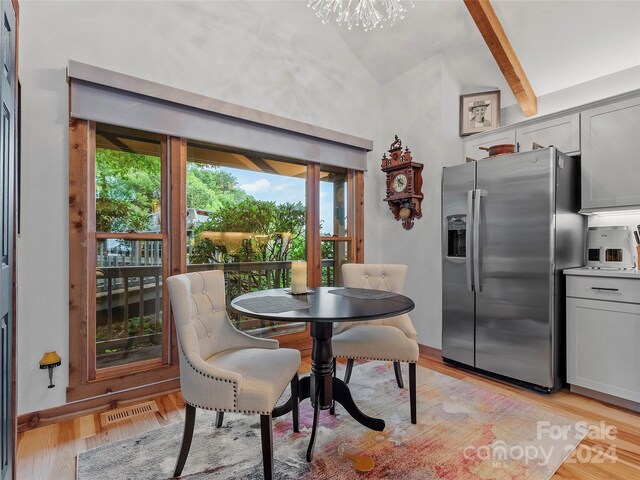 dining space with vaulted ceiling with beams, a healthy amount of sunlight, a chandelier, and light hardwood / wood-style floors