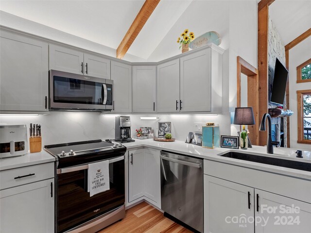 kitchen with lofted ceiling with beams, light wood-type flooring, stainless steel appliances, and sink