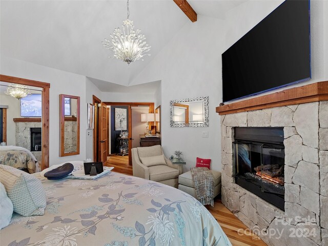 bedroom with light hardwood / wood-style flooring, a stone fireplace, lofted ceiling with beams, and an inviting chandelier