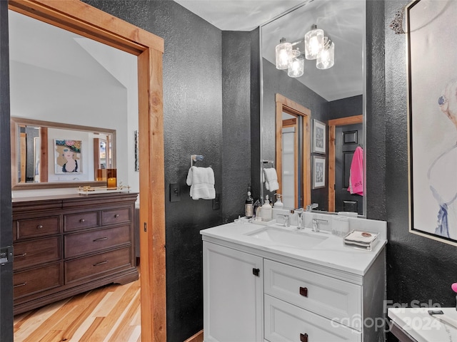 full bath with a textured wall, two vanities, a sink, and wood finished floors