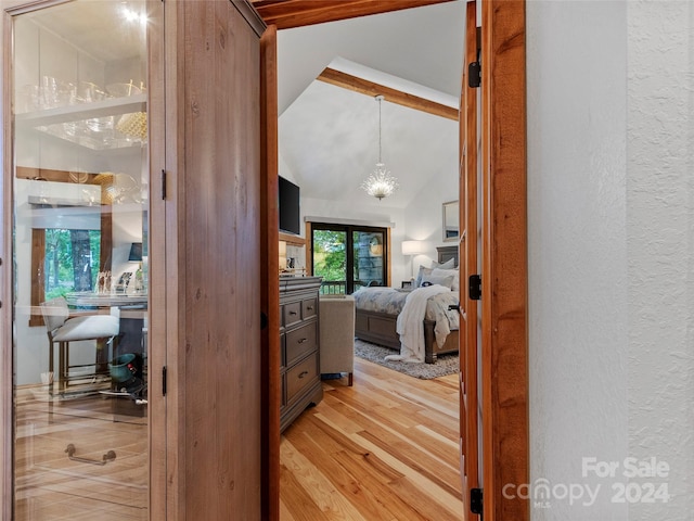 bedroom featuring light wood-type flooring, a textured wall, and lofted ceiling with beams