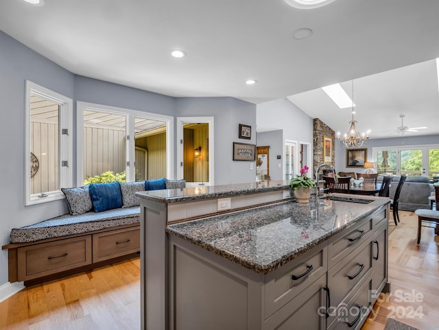 kitchen featuring dark stone countertops, sink, a center island with sink, and vaulted ceiling