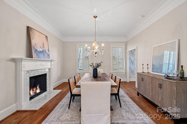 dining space with a fireplace, wood-type flooring, ornamental molding, and a chandelier