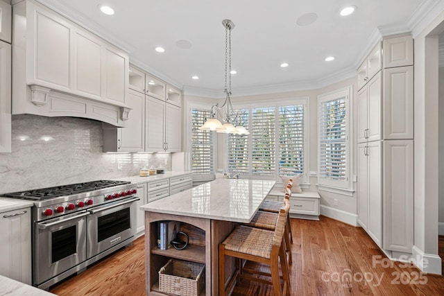 kitchen with a center island, ornamental molding, light hardwood / wood-style floors, range with two ovens, and white cabinets