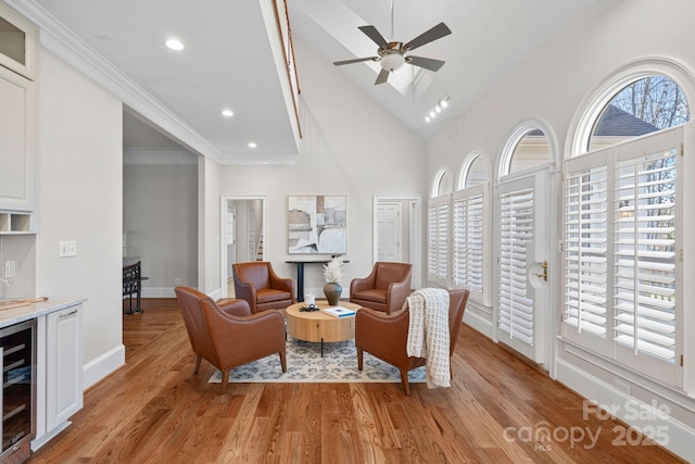 living room featuring high vaulted ceiling, beverage cooler, ornamental molding, ceiling fan, and light hardwood / wood-style flooring