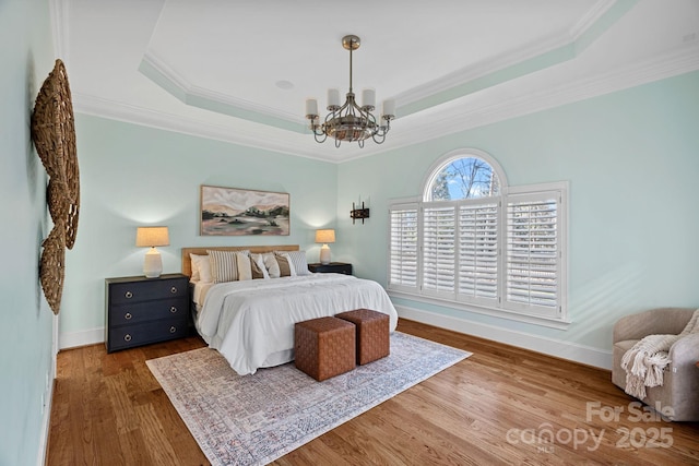 bedroom with a notable chandelier, crown molding, wood-type flooring, and a raised ceiling