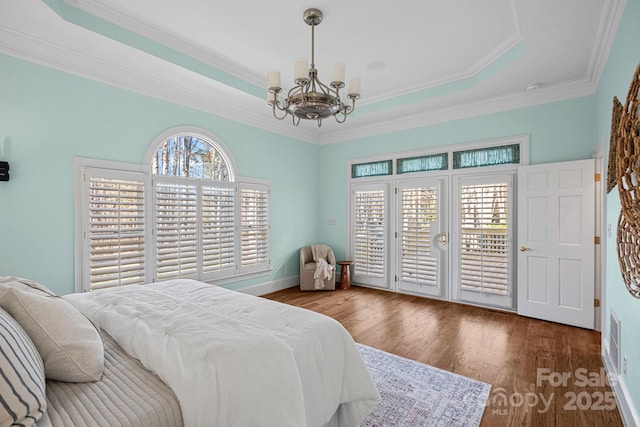 bedroom with multiple windows, a tray ceiling, wood-type flooring, and a chandelier