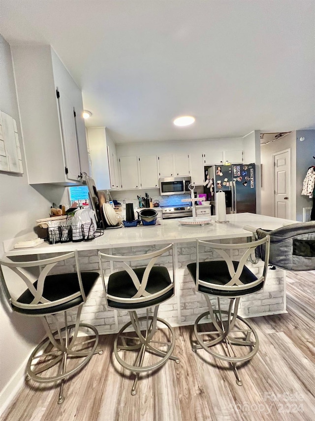 kitchen featuring stainless steel appliances, a breakfast bar, white cabinets, and light hardwood / wood-style flooring