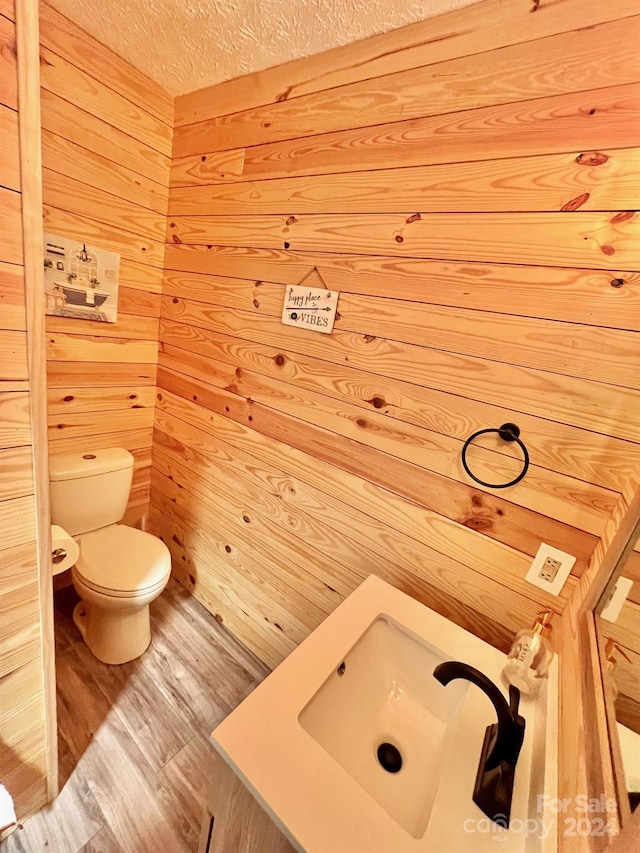 bathroom featuring toilet, sink, a textured ceiling, wooden walls, and hardwood / wood-style flooring