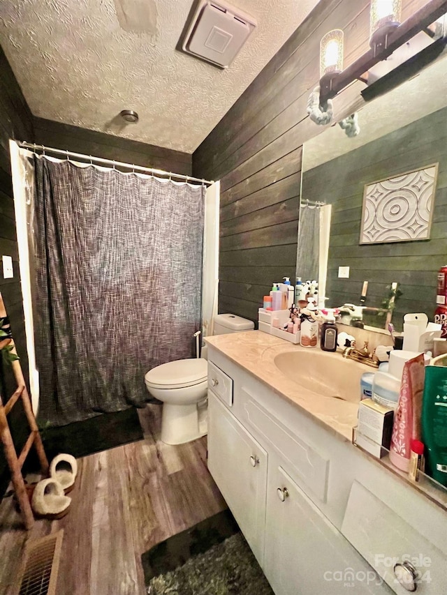 bathroom featuring toilet, a textured ceiling, vanity, wooden walls, and hardwood / wood-style floors