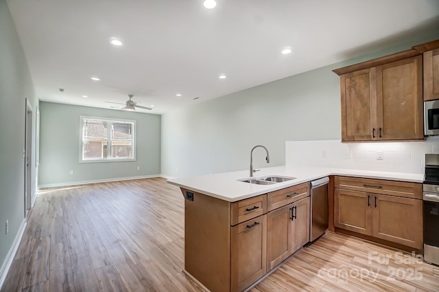 kitchen with kitchen peninsula, appliances with stainless steel finishes, sink, backsplash, and light wood-type flooring