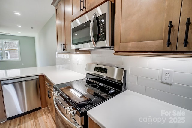 kitchen featuring light hardwood / wood-style flooring, kitchen peninsula, appliances with stainless steel finishes, and decorative backsplash