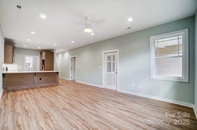 unfurnished living room featuring ceiling fan, sink, and light wood-type flooring