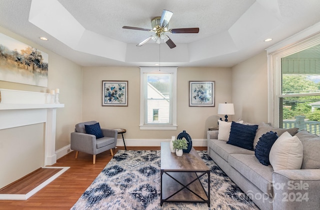 living room with hardwood / wood-style floors, ceiling fan, a tray ceiling, and a healthy amount of sunlight