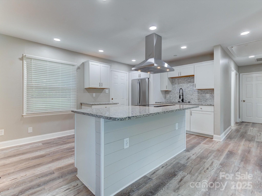 kitchen with a kitchen island, white cabinets, stainless steel refrigerator, and island exhaust hood