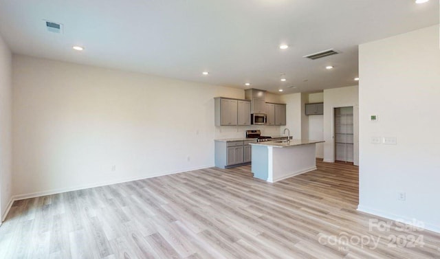 kitchen featuring light wood-type flooring, gray cabinets, stainless steel appliances, and an island with sink