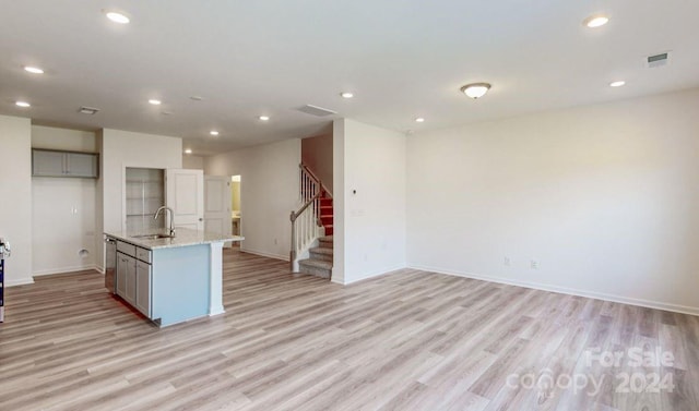 kitchen featuring gray cabinetry, sink, an island with sink, and light wood-type flooring